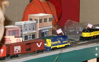 O Scale Trains roll by on this busy layout as the students look on. Buildings in photo were constructed by the students using Model Builder software.